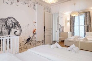 Habitación de hotel con una cama grande, una cuna, un espejo y vista a la ciudad desde la ventana.