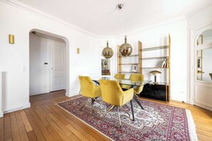 Comedor con mesa de vidrio, sillas amarillas, alfombra estampada y una estantería.