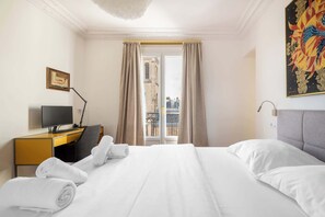 Una habitación de hotel con cama, escritorio con computadora, silla y ventana con cortinas.