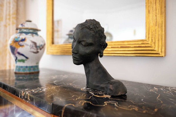A bust sculpture on a marble surface with a decorative vase and a framed mirror in the background.