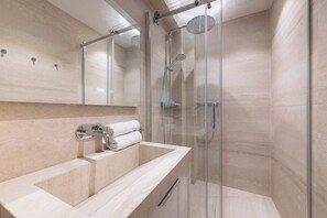 Un baño moderno con ducha de vidrio, lavamanos de mármol y un espejo grande.