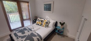 A bedroom with a bed, a nightstand, a window with blinds, a framed picture on the wall, and a small plant on the nightstand. - Elegantly Refurbed 2BD in Shankill - 3km from Bray (Dublin)