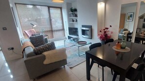 Ein modernes Wohnzimmer mit einer Couch, einem Esstisch, Stühlen, einem Fernseher und einer Küche im Hintergrund.