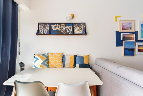 Una habitación moderna con cama, sofá, mesa de comedor y una pared decorada con cuadros.