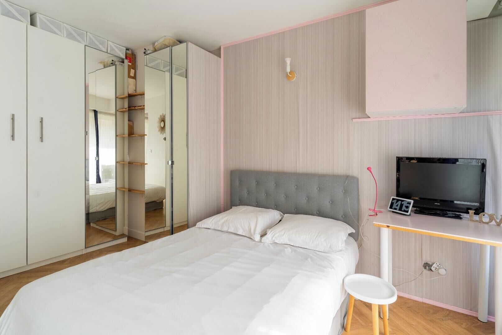 A bedroom with a bed, a TV, a desk, and a wardrobe.