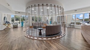 A spacious, modern lounge area with a circular seating arrangement, large windows, and a wooden floor. - ⛱️Ocean View Retreat with Private Balcony | Horizon at 77th - Unit 812🌊 (Myrtle Beach)
