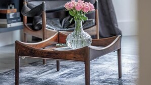 Een houten stoel met een vaas roze bloemen op een geweven vloerkleed.