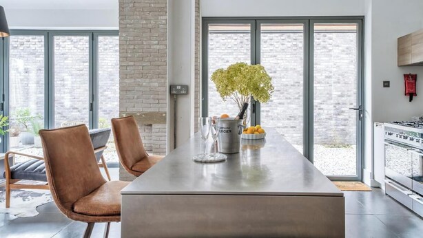 Een moderne keuken met een groot schiereiland, een zithoek met twee stoelen, een groot raam en een metselwerk muur.