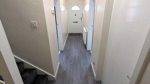 Ein schmaler Flur mit einer Tür am Ende, einem kleinen Fenster und einem Heizkörper an der Wand.