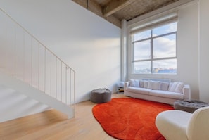 A modern living room with a white staircase, a large window with a city view, a white sofa, and a red rug.