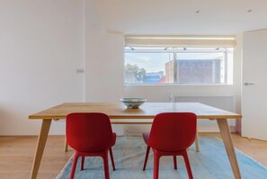 A dining area with a wooden table, two red chairs, a bowl on the table, and a window with a view of buildings.