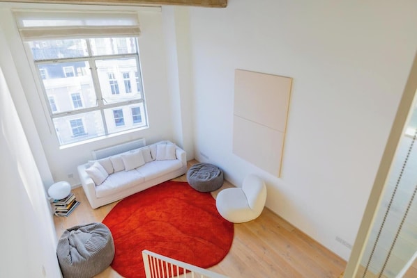 A modern living room with a white sofa, a red rug, and two round bean bags.