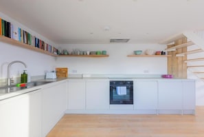 A modern kitchen with white cabinetry, a built-in dishwasher, and wooden shelves above the counter.