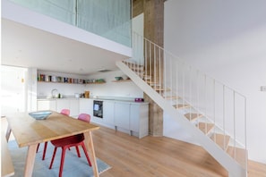 A modern kitchen with white cabinets, a dining area with a wooden table and red chairs, and a staircase with white railings.