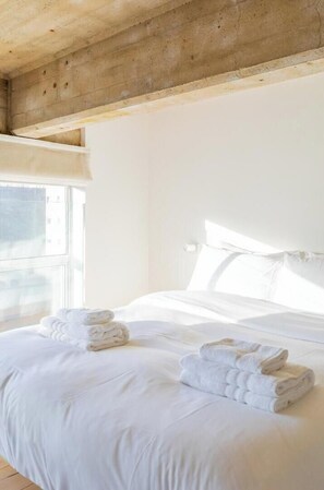 A hotel room with a bed, white linens, a window, and a wooden ceiling.