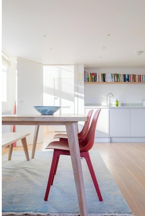 A modern kitchen with a dining area, featuring a wooden table, red chairs, and a blue bowl on the table.