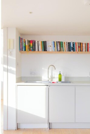 A modern kitchen with a built-in bookshelf, a sink, and a green soap dispenser. - Chic 1BD Warehouse Conversion, Hackney (Greater London)