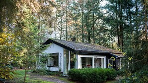 Una pequeña casa con techo de tejas, rodeada de un bosque frondoso.