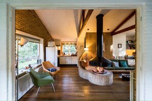 Een gezellige woonkamer met een open haard, houten vloeren en uitzicht op de keuken.