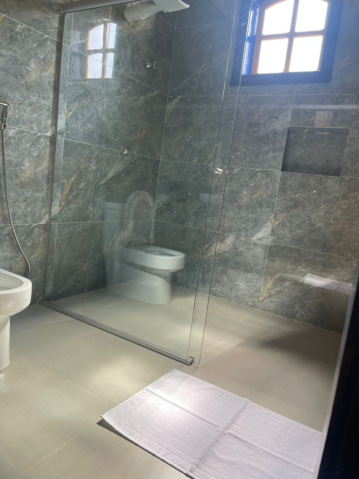 Een moderne badkamer met een glazen douchecabine, toilet en wastafel.