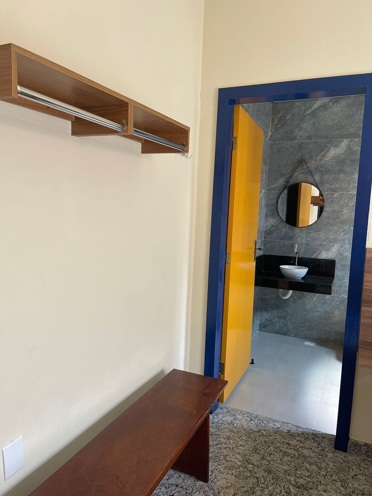 A hallway with a wooden bench, a mirror, and a bathroom with a sink and mirror.