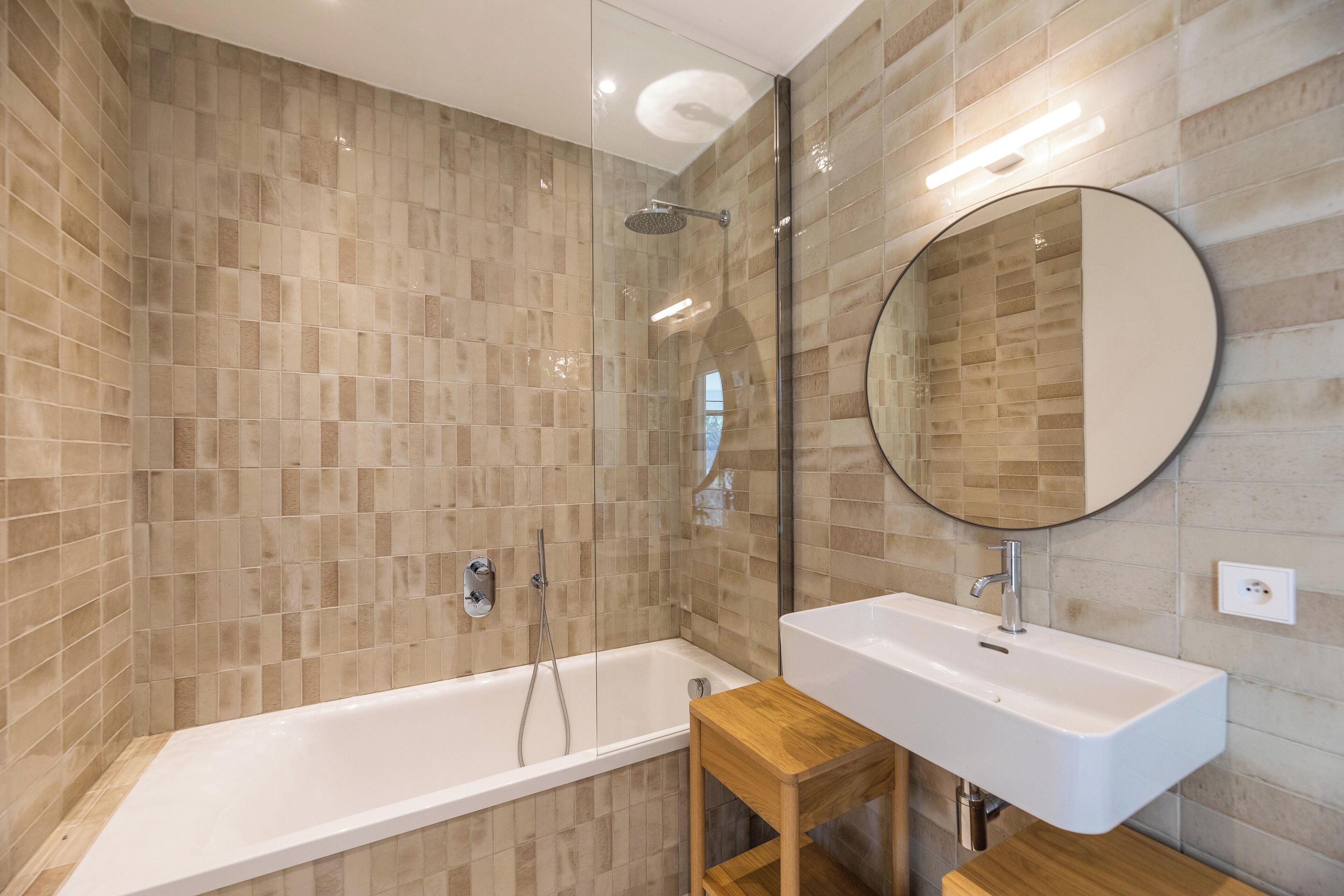 A modern bathroom with a glass-enclosed shower, a white bathtub, and a wooden vanity with a sink.