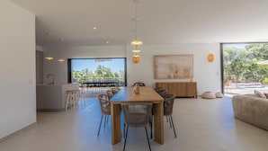 Een ruime woonkamer met een eettafel, stoelen, een bank en een keukenhoek.