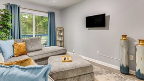 Un salon moderne avec un canapé gris, un pouf et un téléviseur à écran plat fixé au mur.