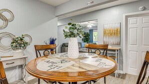 Un coin repas avec une table ronde en bois, des chaises et un vase blanc orné de verdure.