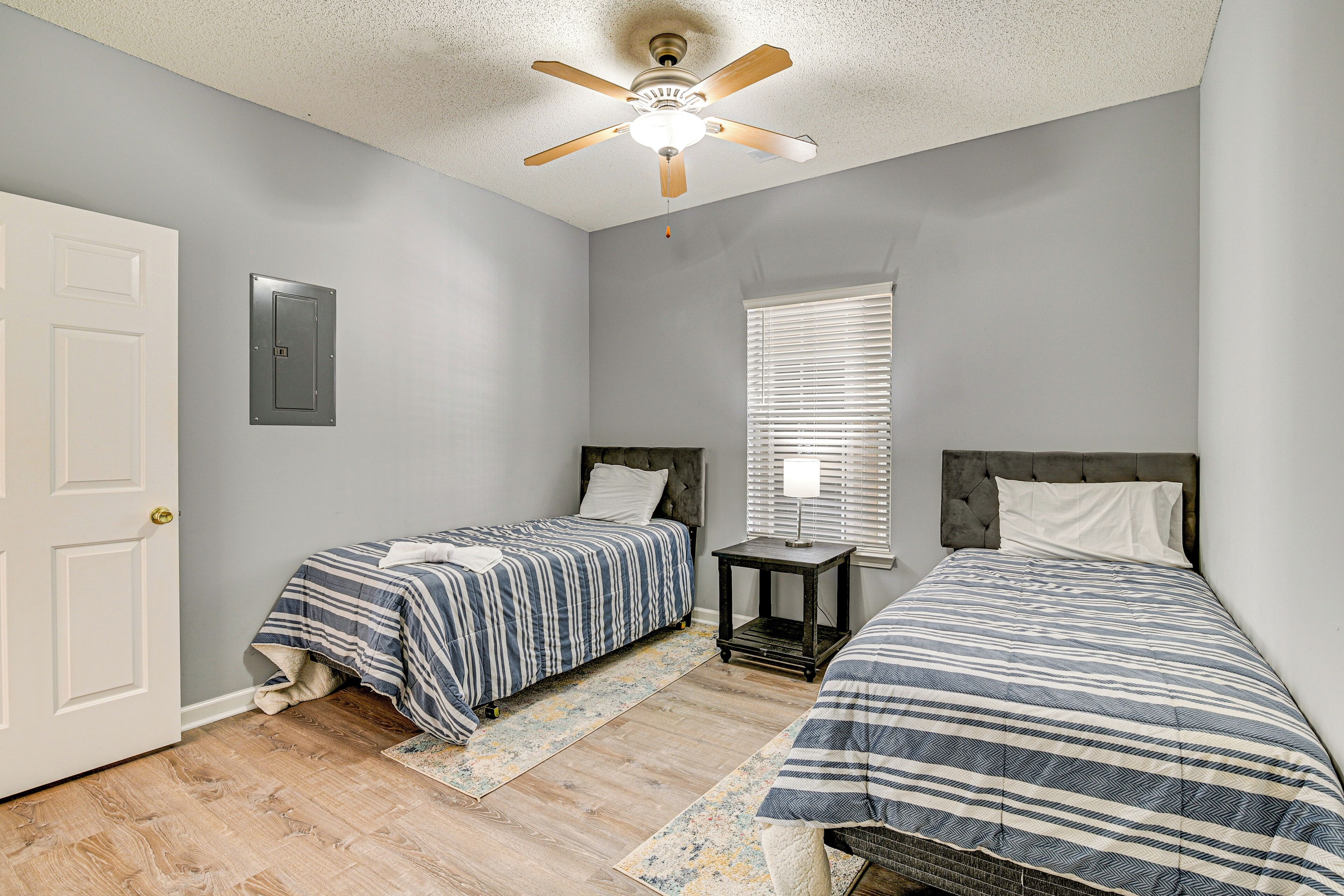 A bedroom with two beds, a ceiling fan, a window with blinds, and a door.