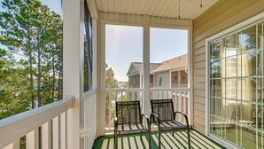 A covered porch with two chairs and a table, overlooking a residential area with houses and trees. - Pool + Hot Tub: Lake-view Condo in Surfside Beach! (Surfside Beach)