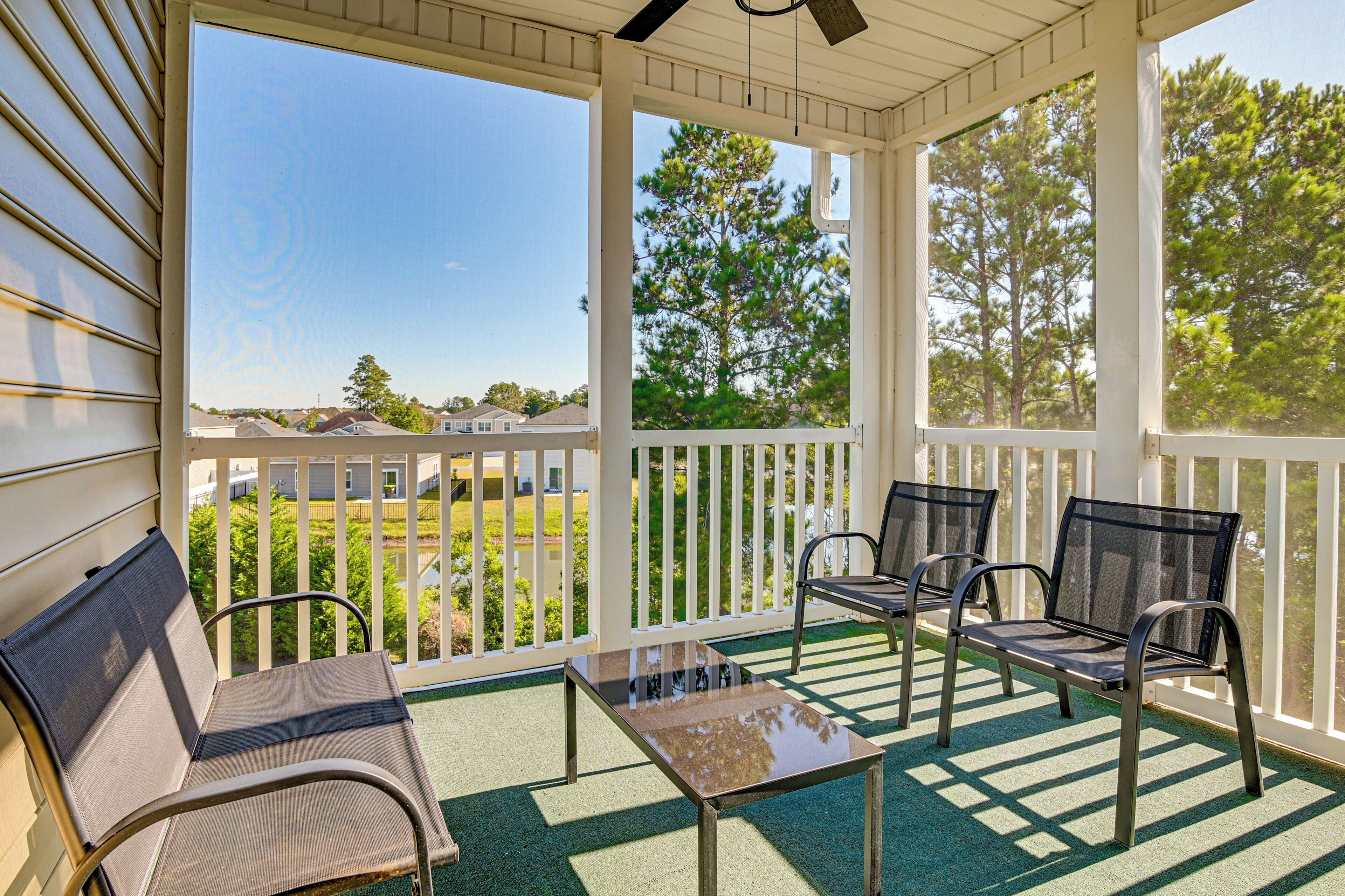A covered porch with two chairs and a table, overlooking a residential area with houses and trees.