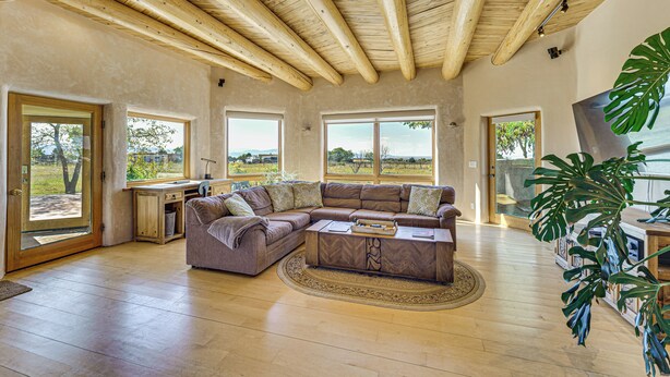 A spacious living room with a large L-shaped sectional sofa, wooden flooring, and a high ceiling with exposed beams. - 10 Mi to Taos Ski Valley: Mtn-view Duplex w/ Deck! (Arroyo Seco)