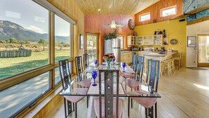 A spacious dining area with a large glass table and chairs, a kitchen in the background, and a view of the outdoors. - 10 Mi to Taos Ski Valley: Mtn-view Duplex w/ Deck! (Arroyo Seco)