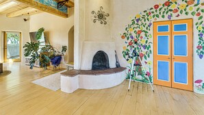 A spacious room with a fireplace, wooden beams, and a colorful floral mural. - 10 Mi to Taos Ski Valley: Mtn-view Duplex w/ Deck! (Arroyo Seco)