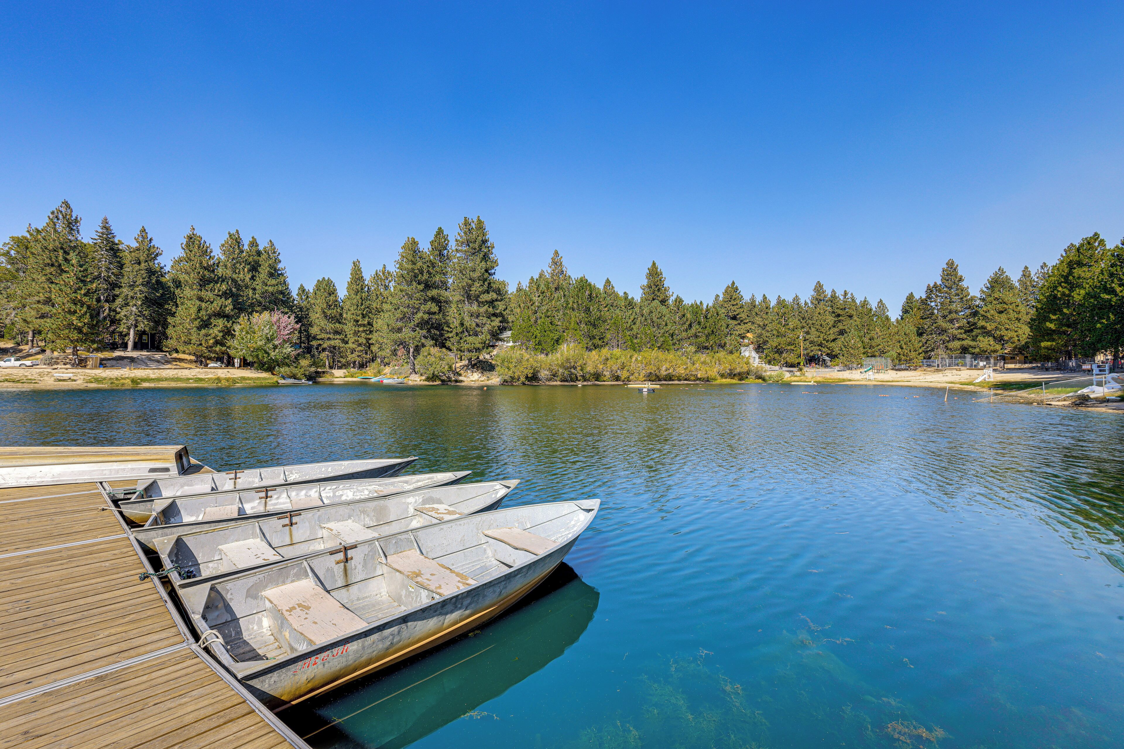 A wooden dock with several boats moored at the edge of a calm lake, surrounded by dense trees and clear skies.
