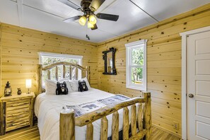 A wooden cabin bedroom with a bed, a nightstand, a ceiling fan, and a window. - Walk to Water: Cozy Cabin in Green Valley Lake! (Green Valley Lake)
