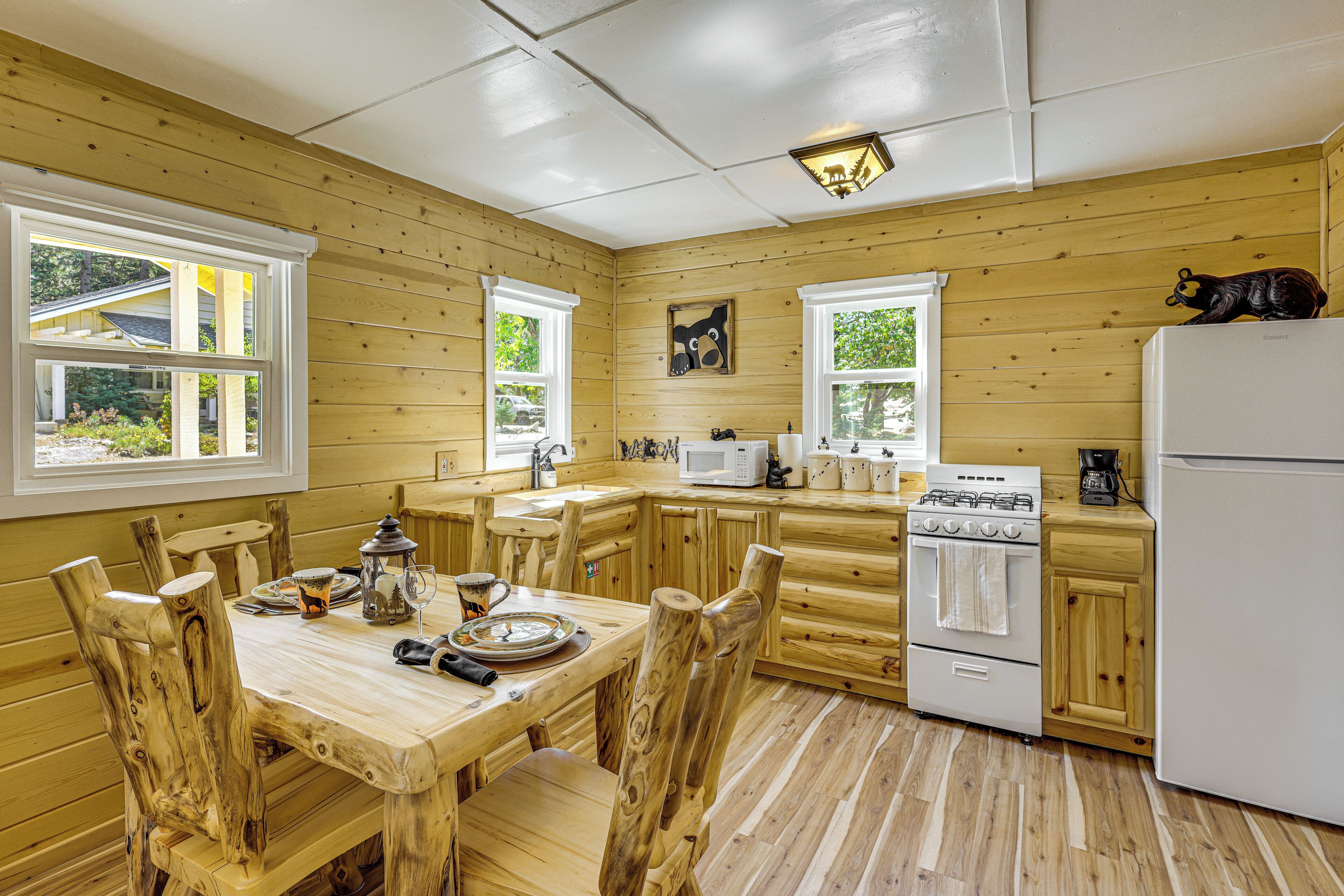 A wooden cabin kitchen with a dining table, chairs, a stove, a refrigerator, and a microwave.