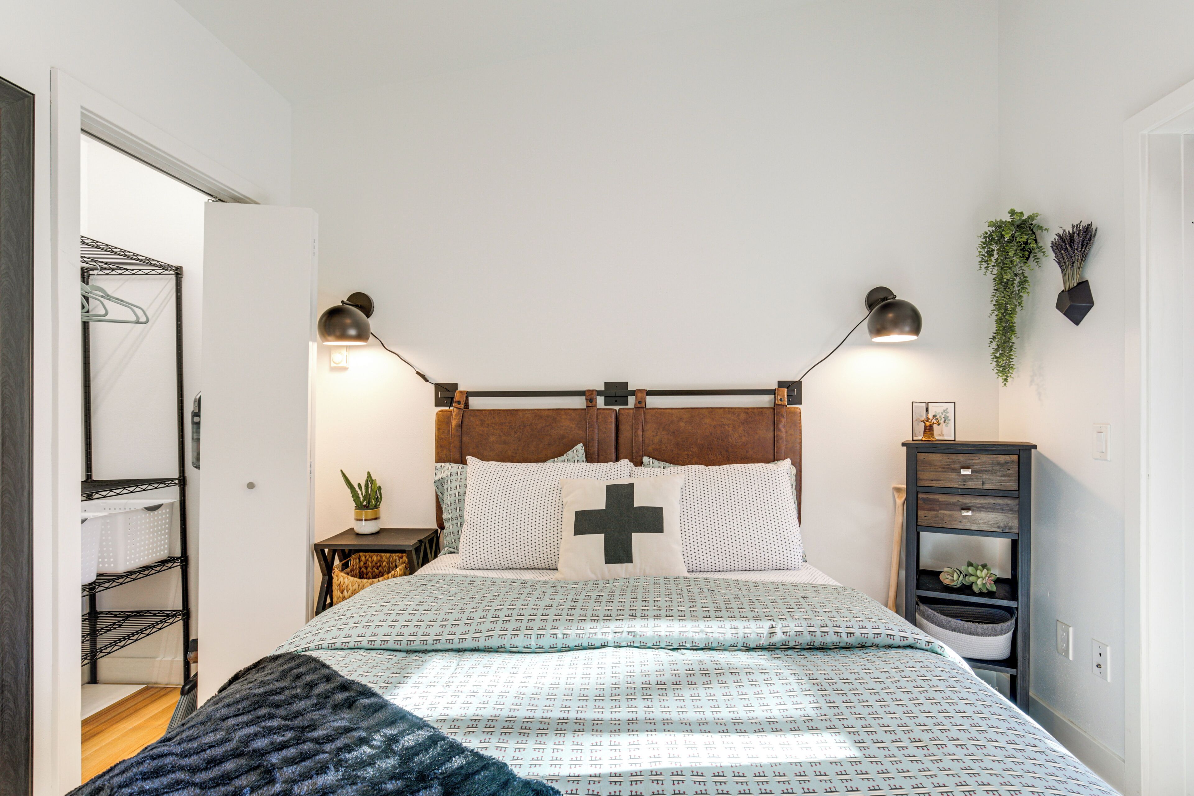 Een keurig opgemaakte slaapkamer met een bed, bedlampen, een plantje en een wandplank.