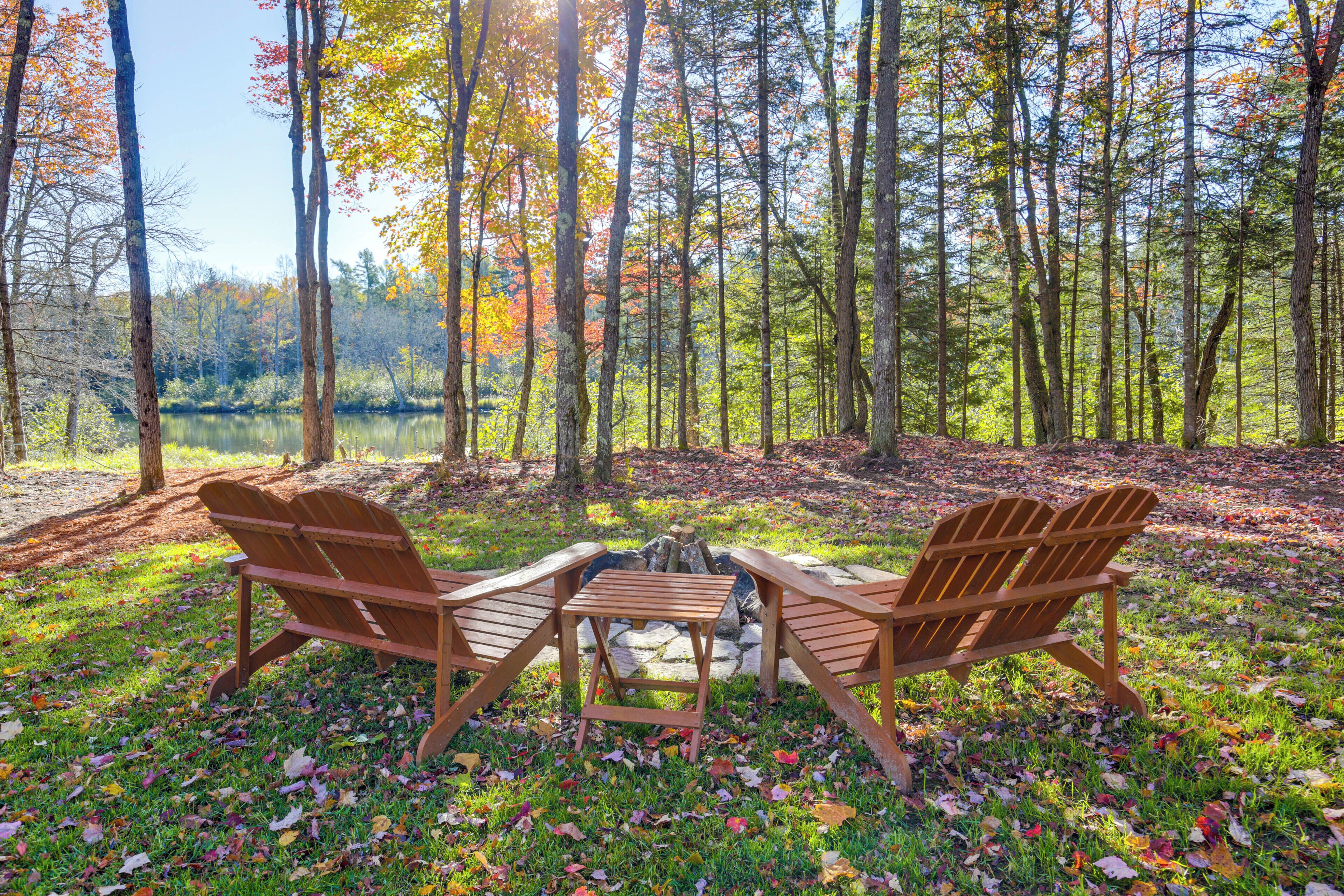 Una mesa de madera y dos sillas en un claro del bosque con un lago al fondo.