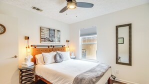 Un dormitorio con cama, ventilador de techo, ventana, espejo y una obra de arte colgada en la pared.