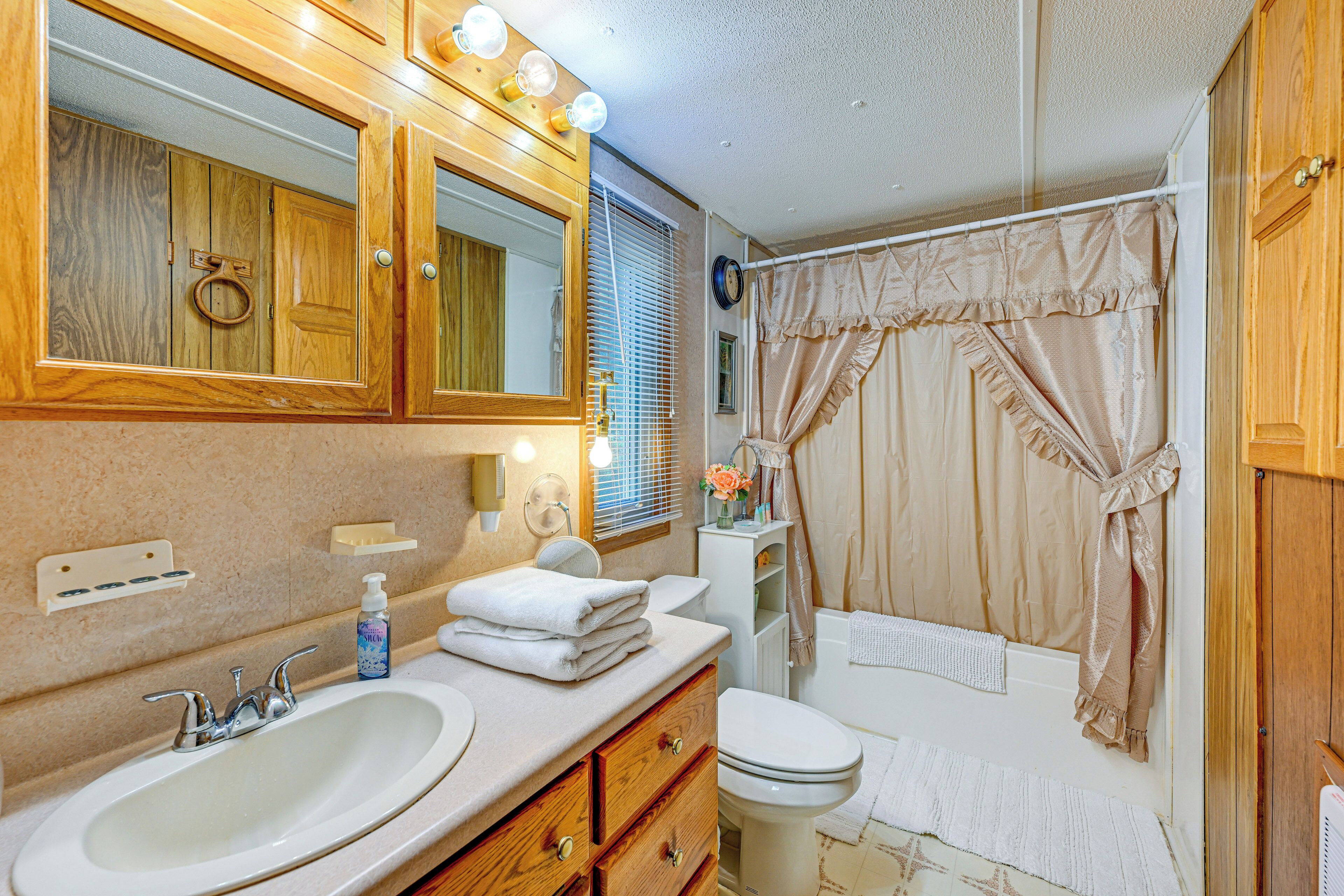 A bathroom with wooden cabinets, a sink, a toilet, and a shower area.