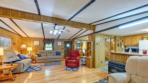A cozy living room with wooden floors, a fireplace, a sofa, a recliner, and a kitchen area with wooden cabinets and a microwave. - Creek Access & Spacious Yard: Quiet Sylva Home! (Sylva)