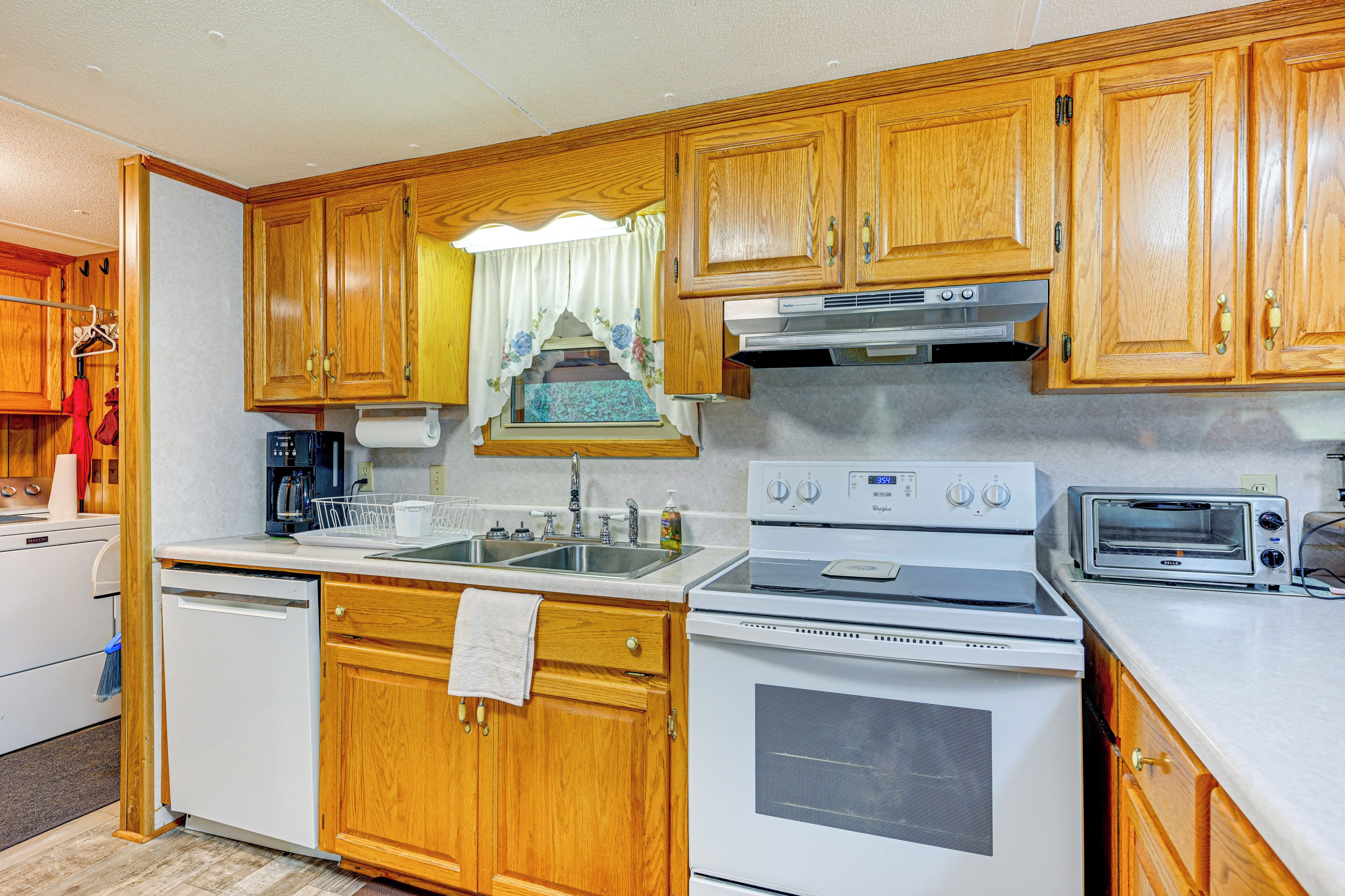 A kitchen with wooden cabinets, a white dishwasher, a stove, a sink, and a toaster.
