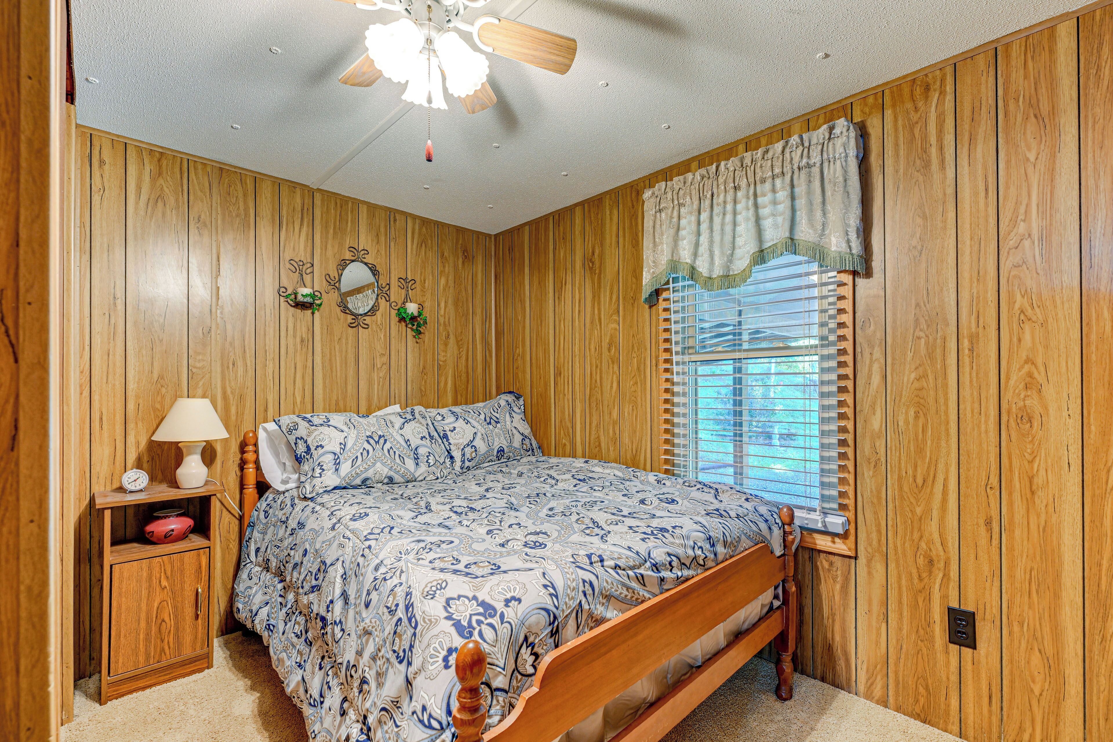 Ein Schlafzimmer mit Holzwandverkleidung, einem Bett mit gemustertem Überwurf, einem Nachttisch mit Lampe und einem Fenster mit Jalousien.