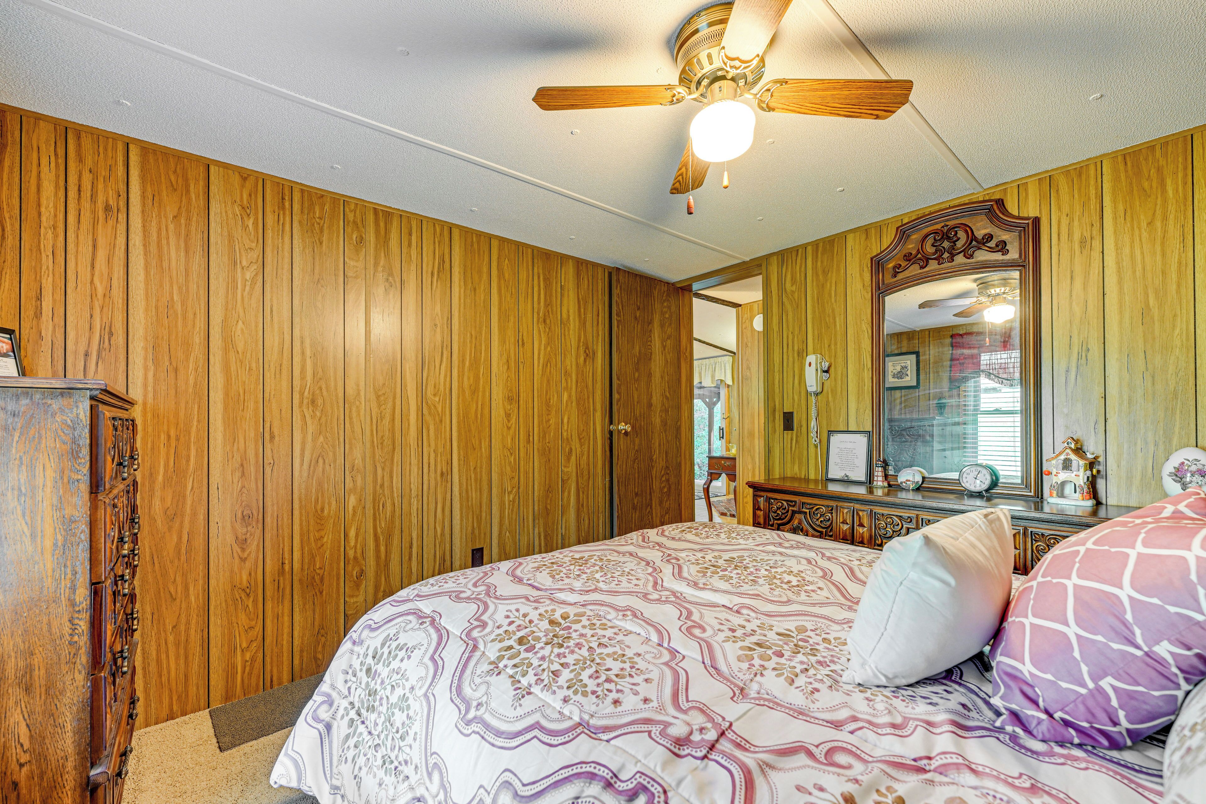 A bedroom with wooden panel walls, a ceiling fan, a bed with patterned bedding, and a dresser.