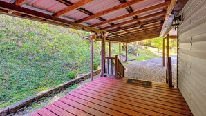 A wooden deck with a metal roof, a stone wall, and a gravel path leading to a building. - Creek Access & Spacious Yard: Quiet Sylva Home! (Sylva)