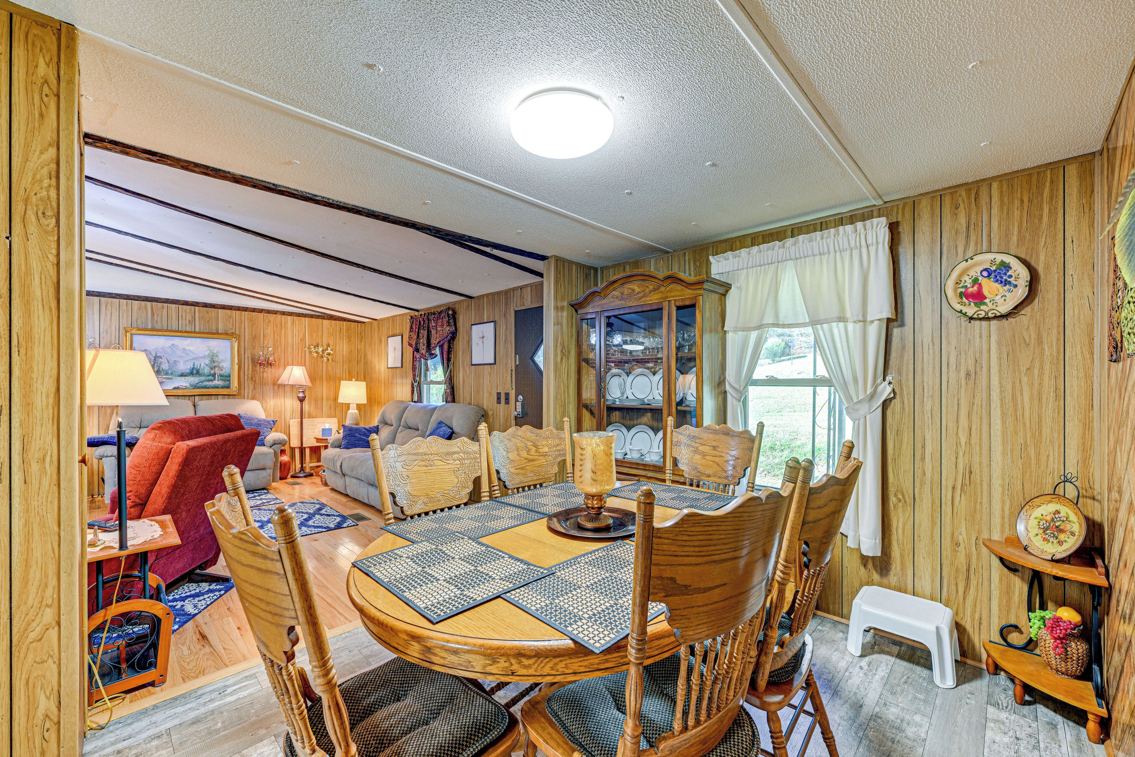 A cozy living room with a dining area, wooden walls, and a large window.
