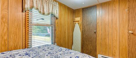 A bedroom with wooden paneling, a patterned bedspread, a window with blinds, and a ceiling light fixture.