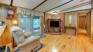A living room with a fireplace, wooden flooring, a sofa, a clock, and a TV. - Creek Access & Spacious Yard: Quiet Sylva Home! (Sylva)